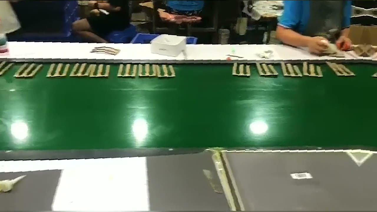 Foil-stamped card blanks laid out along a green conveyor while operators collate and inspect them, filmed on the floor of a factory in the TruePack network.